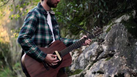 músico folclórico tocando música con guitarra acústica en un bosque verde