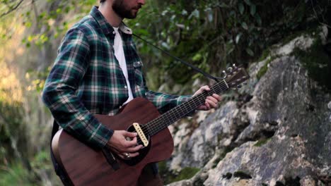 folk mussician playin music with acoustic guitar in a green forest