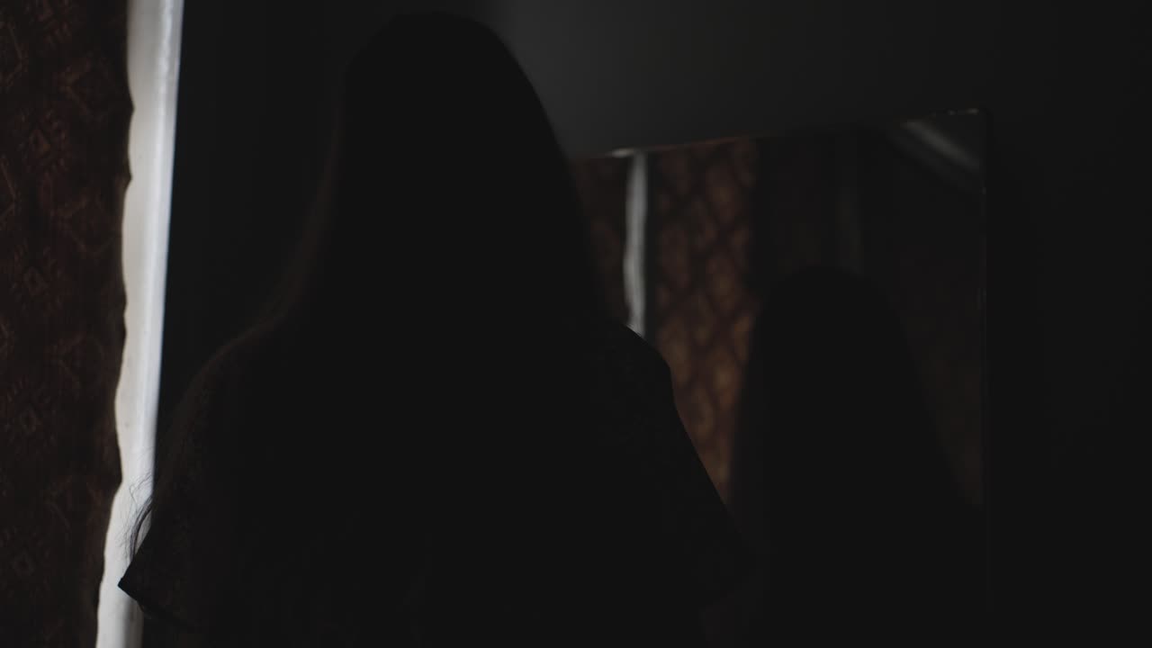 Dark cinematic Halloween shot featuring a possessed woman staring into an antique mirror in a haunted setting. Perfect for horror intros, thriller trailers, or supernatural themed