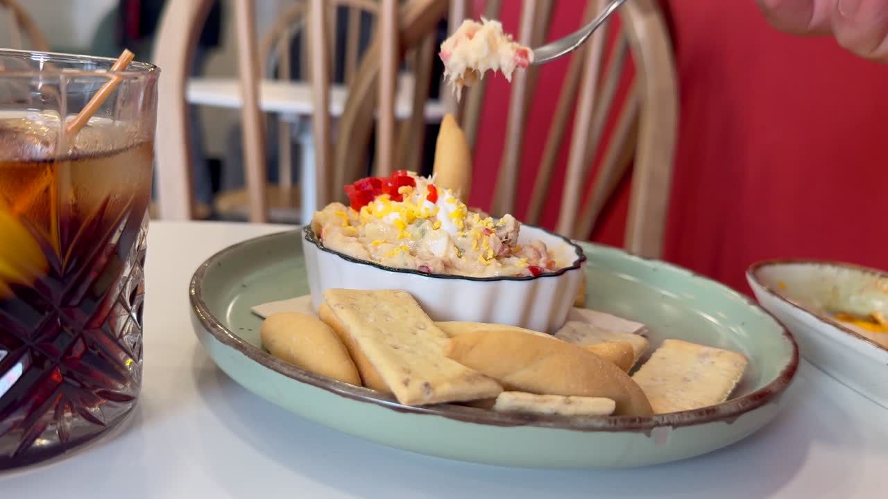 Primer plano de la mano de un hombre caucásico comiendo ensaladilla rusa casera con un tenedor en un bar español tradicional.