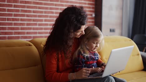 madre e hija sentadas en el sofá y escribiendo en la computadora portátil juntas