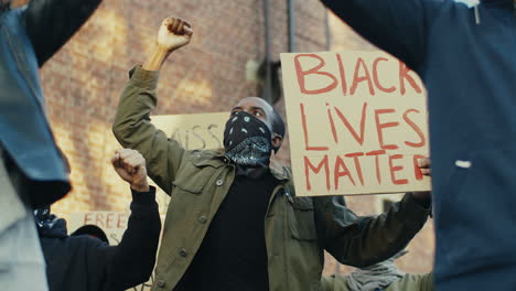 hombre afroamericano gritando y sosteniendo vidas negras importan" cartel en una protesta con un grupo multiétnico de personas en la calle"