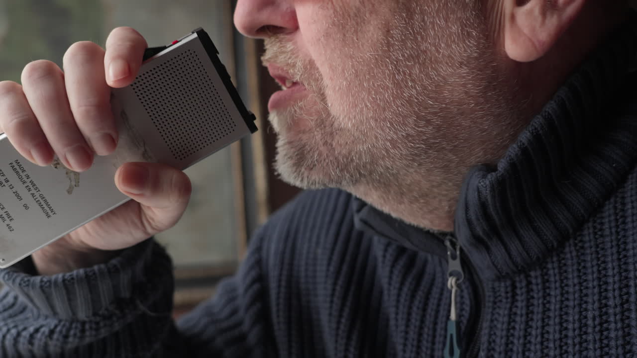 En mand taler med følelsesmæssig intensitet ind i en vintage analog stemmeoptager. Filmisk profiloptagelse til vintage kommunikation og true crime-fortællinger