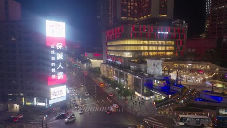 night scene in taipei with traffic on junction near shopping mall at night, taiwan. flashing advertising panel in city center. aerial tilt down shot.