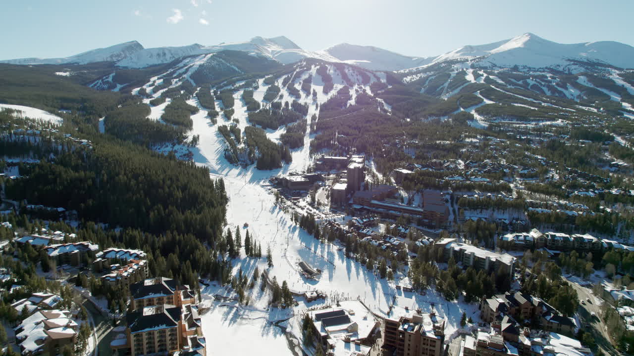 An aerial view over the popular Breckenridge ski resort in Colorado, with snow covered mountain peaks and high altitude trails full of winter skiers and snowboarders on a sunny winter day.