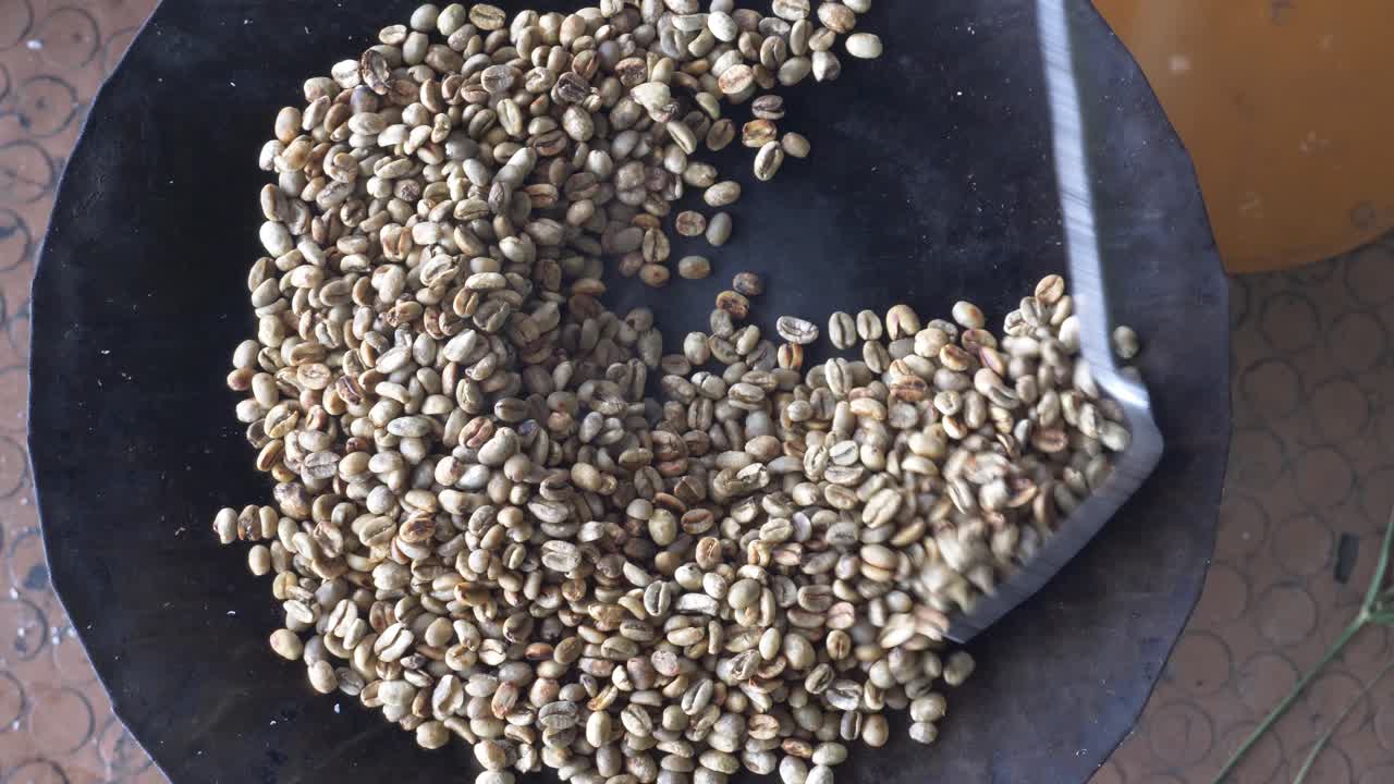 Ripresa dall'alto di chicchi di caffè durante la tostatura su una piastra metallica; questo è l'inizio del processo e i chicchi sono ancora verdi.