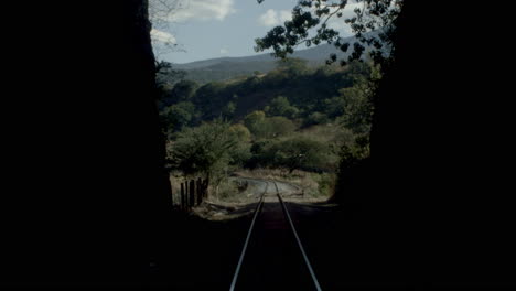 point of view of a train moving over railroad tracks alongside the country and crossing a tunnel