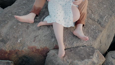 ein ehepaar sitzt auf felsen am strand von ovar (portugal) und konzentriert sich auf ihre beine und ihre bloßen füße