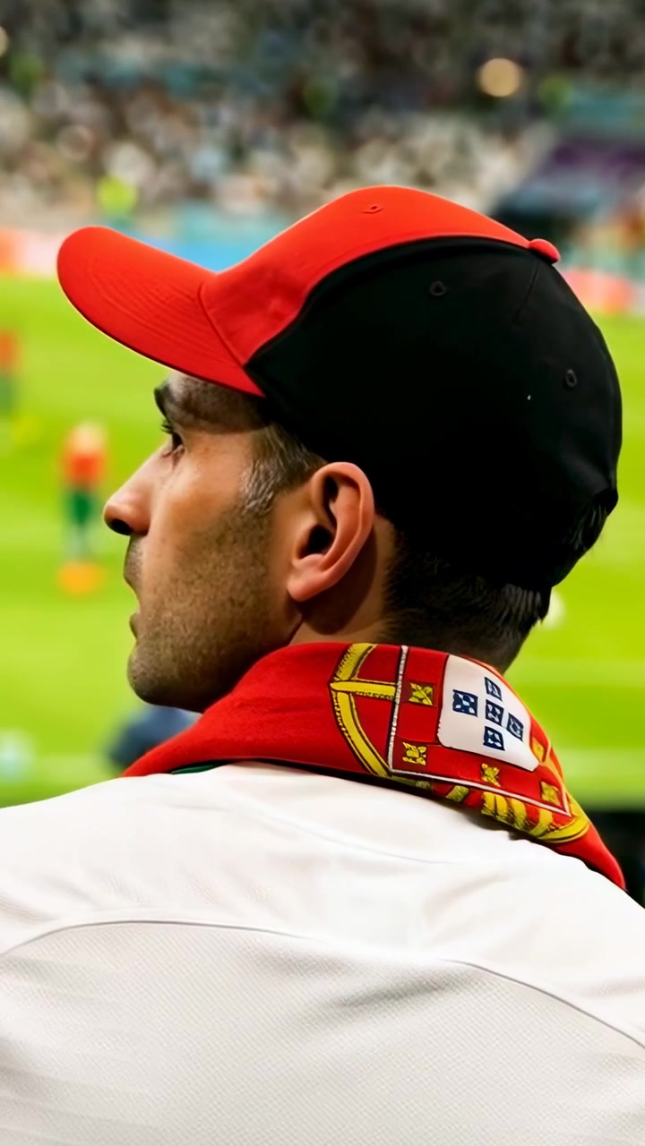 Video verticale: Zoom in su tifoso con cappellino rosso-nero e sciarpa rossa che si gira e segue il gioco dagli spalti.