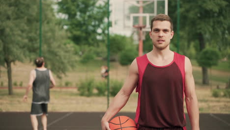 in foreground, an handsome basketball player with ball, breathing heavily after a good productive training session, while looking at camera and smiling confidently 1