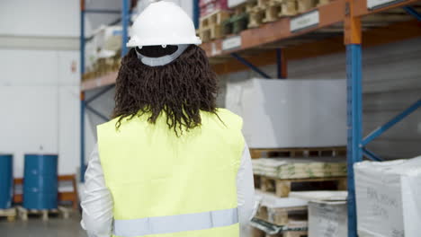 back view of an african american female worker in helmet counting goods in stock