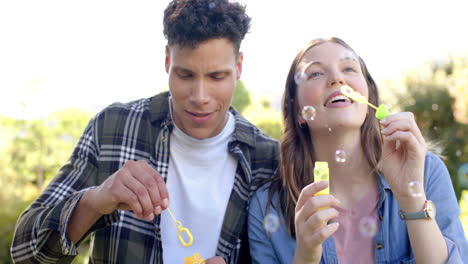 Happy-diverse-couple-blowing-bubbles-in-sunny-garden,-in-slow-motion