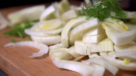 chef grabs handful of chopped fennel from wooden board in kitchen