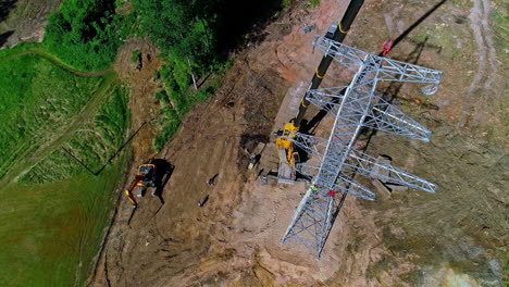 crew of workmen working on a electrical transmission tower with a crane - aerial overlook