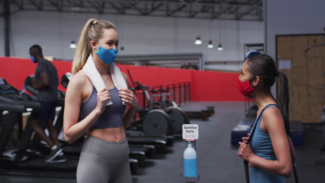 two fit caucasian women wearing face mask greeting each other by touching elbows in the gym