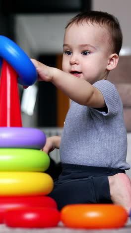 one year old boy constructing a toy pyramid. baby boy playing at home. living room backdrop. vertical video