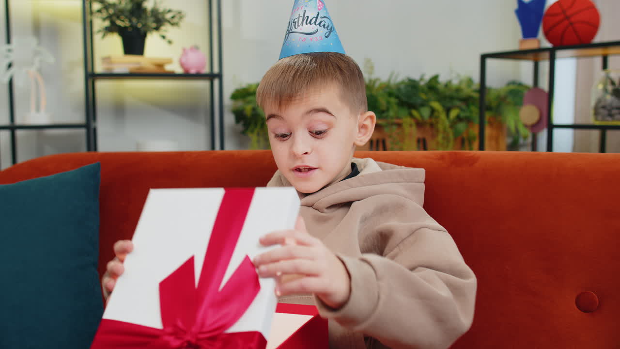 Happy child boy kid hold birthday gift box with ribbon celebrating party opening present at home