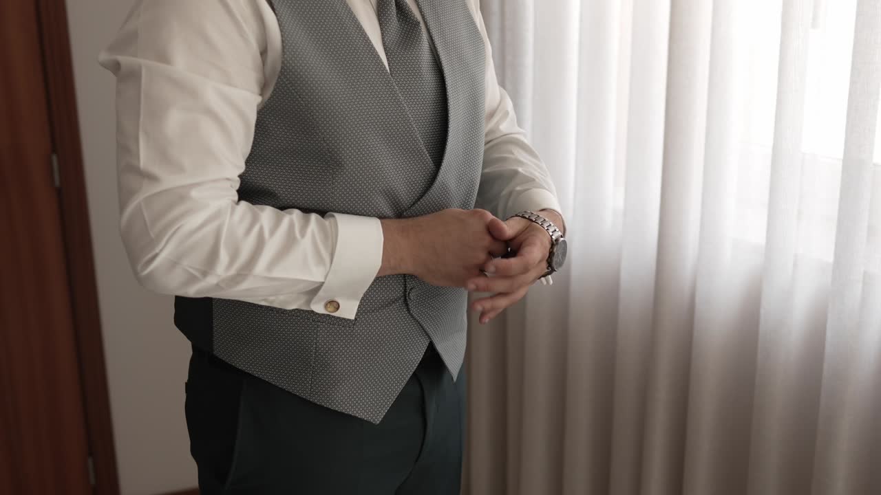close up of groom putting on watch beside a window in soft daylight