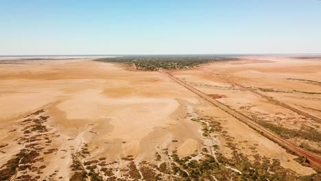 Long-wide-aerial-shot-of-expansive-barren-wasteland-surrounding-bustling-town-in-middle-on-no-where