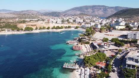 Ksamil,-Albania---Aerial-of-Holiday-Destination-with-Jetski,-Clear-Blue-Sea,-Beach,-Hotels-and-Sunbeds