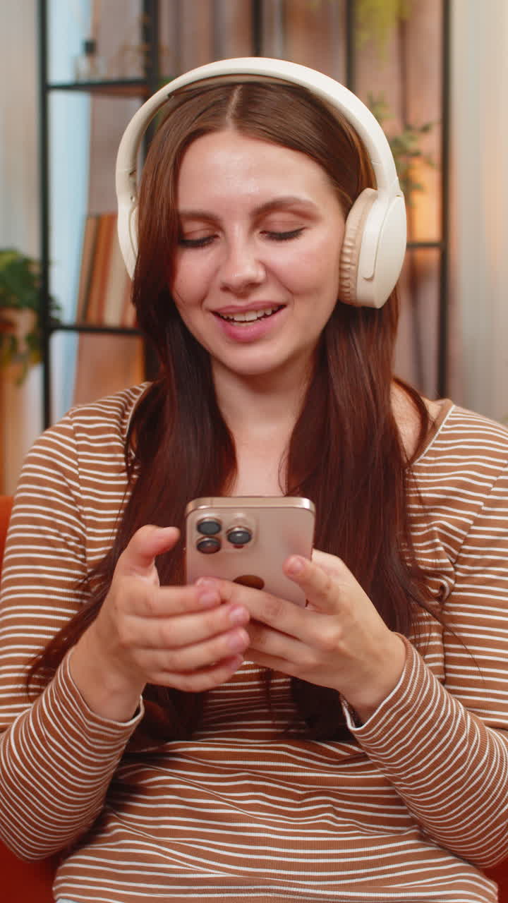 Giovane donna con cuffie wireless avvia una playlist, annuisce a ritmo di musica, sorride e risponde sullo smartphone