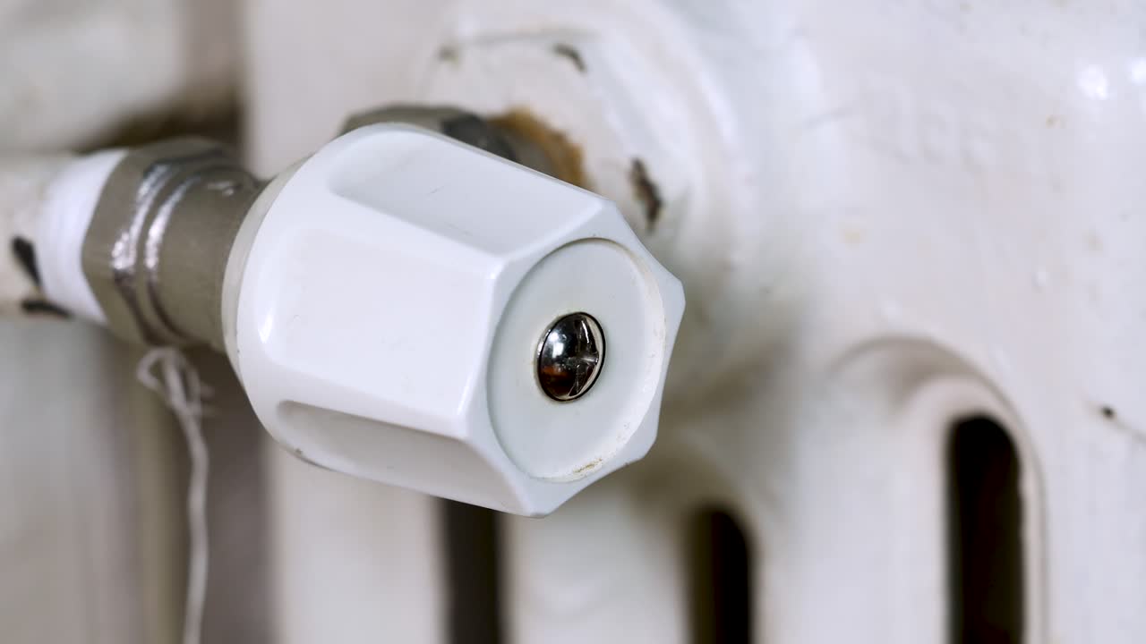 mano masculina cerrando la válvula termostática de un viejo radiador blanco, macro del concepto de precios de gas en 4k