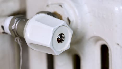mano masculina cerrando la válvula termostática de un viejo radiador blanco, macro del concepto de precios de gas en 4k