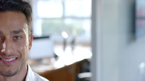 Half-portrait-of-happy-biracial-businessman-smiling-at-office,-with-copy-space,-in-slow-motion