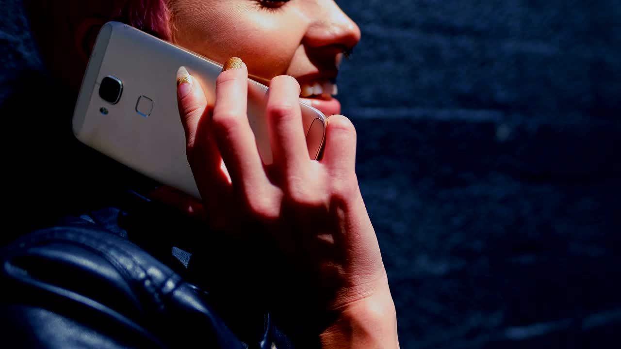 장미 머리카락의 여성이 골목 4k에서 휴대 전화로 이야기하고 있습니다.