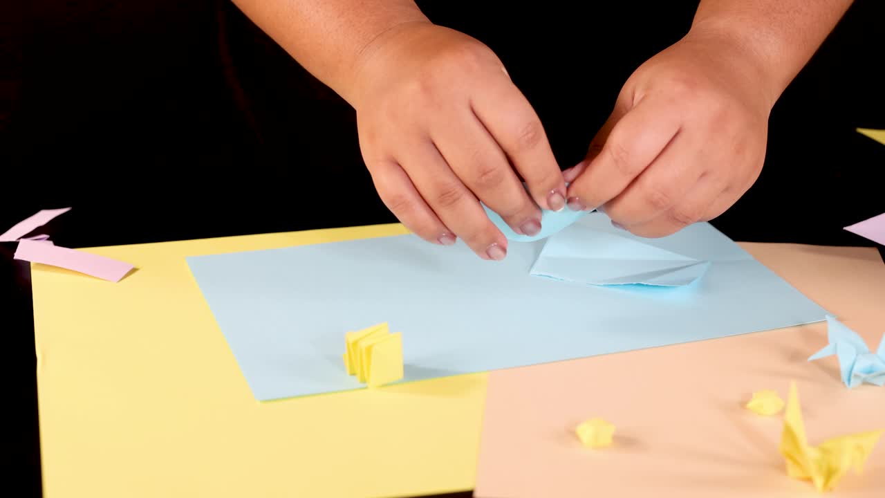 Person tears blue paper by hand on colorful table, under bright lighting, close-up view