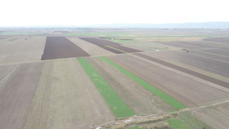 Drone-Camera-Pan-over-Brown-and-Green-Agricultural-Farmland,-daytime,-Aerial