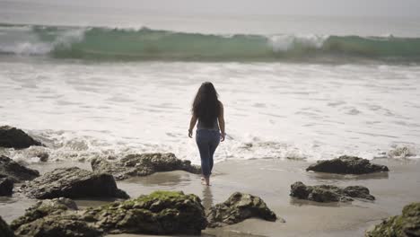 girl walking through water and sand on el matador beach in southern california near malibu - wide shot