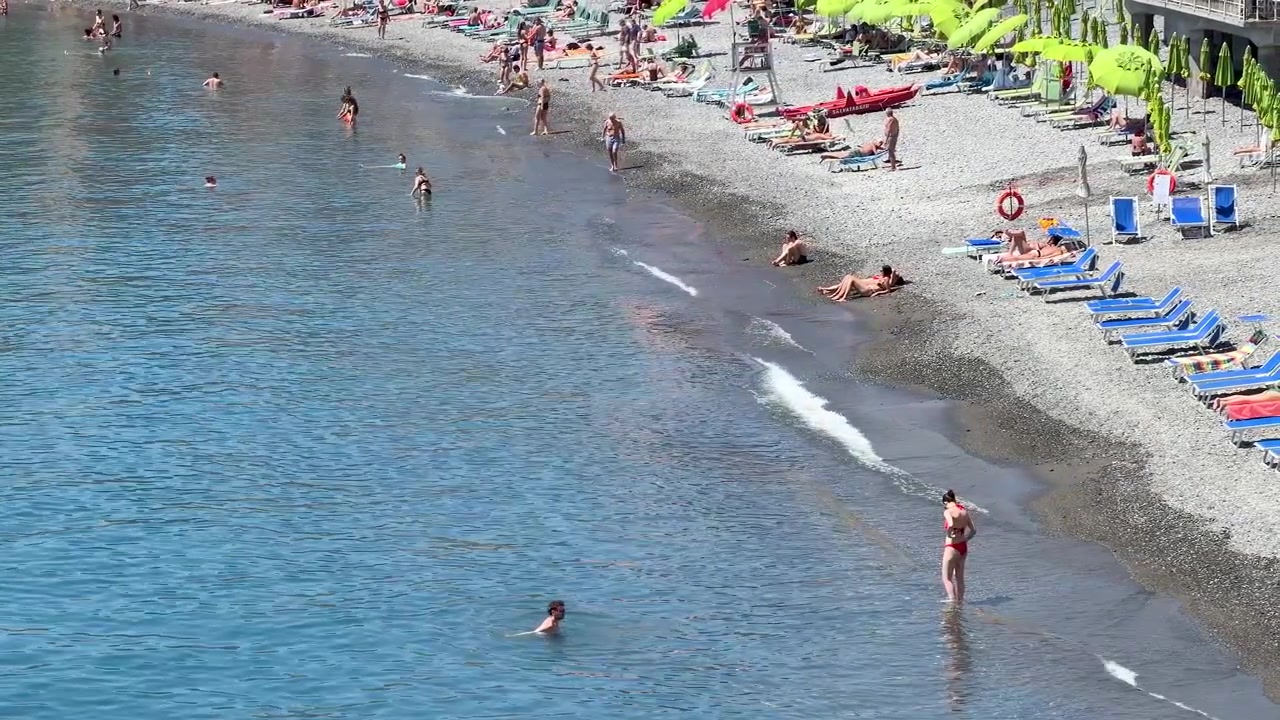 Akdeniz'deki çakıllı bir plajda yüzen ve güneşlenen insanların kuşbakışı görüntüsü.