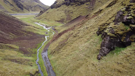 The-aerial-reveal-of-rocky-mountainside-closing-a-green-valley-with-a-river