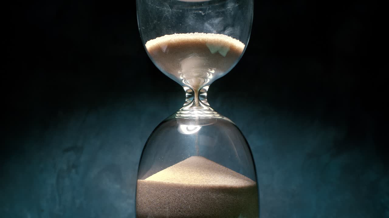 Hourglass with grains of sand on a dark background. Shot on super slow motion camera 1000 fps.