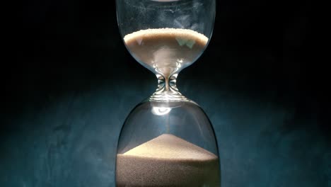 hourglass with grains of sand on a dark background. shot on super slow motion camera 1000 fps.