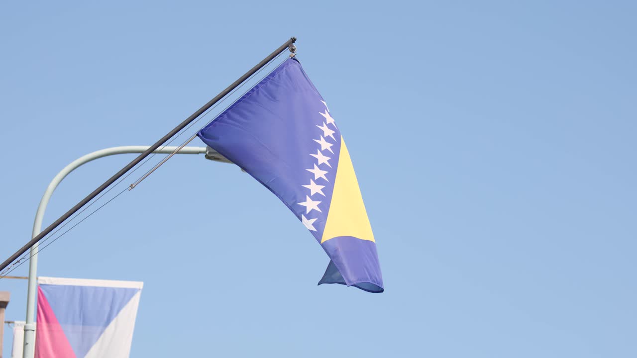 Bosnia and Herzegovina flag waving in wind, clear sky, city street, daylight, static camera