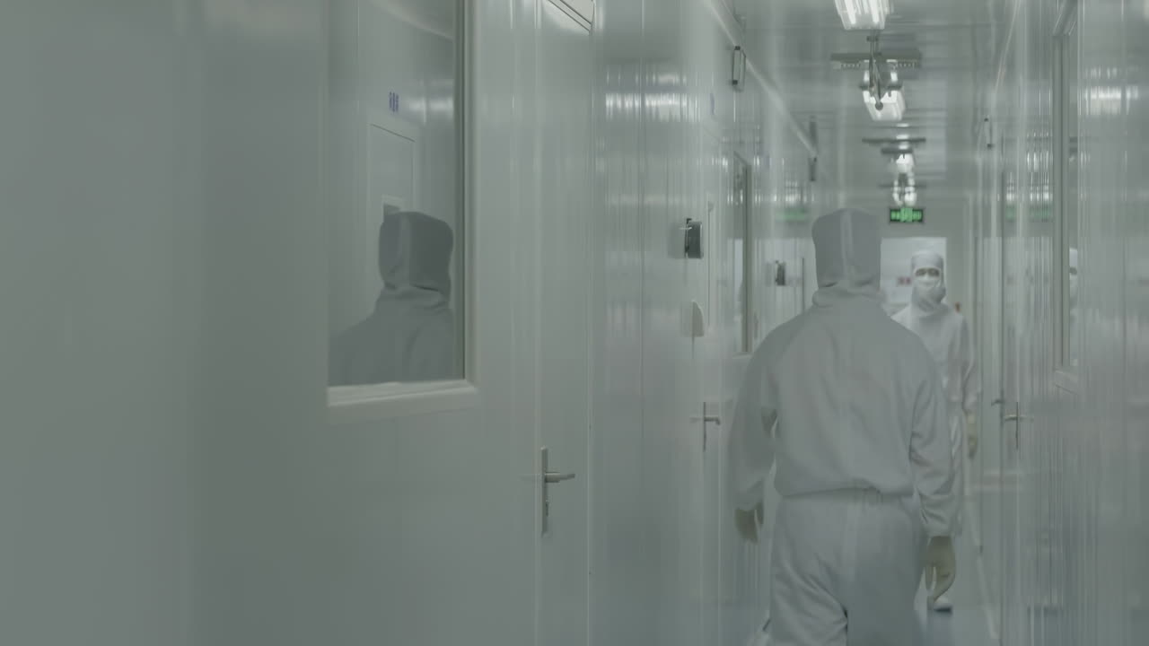 Medical Scientists or researchers equipped with protective suits, face masks, shoe covers and safety goggles, walking in laboratory sterile corridor, exuding a sense of safety and caution