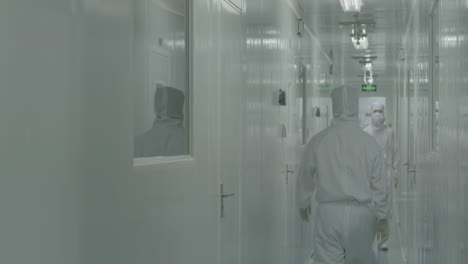 medical scientists or researchers equipped with protective suits, face masks, shoe covers and safety goggles, walking in laboratory sterile corridor, exuding a sense of safety and caution
