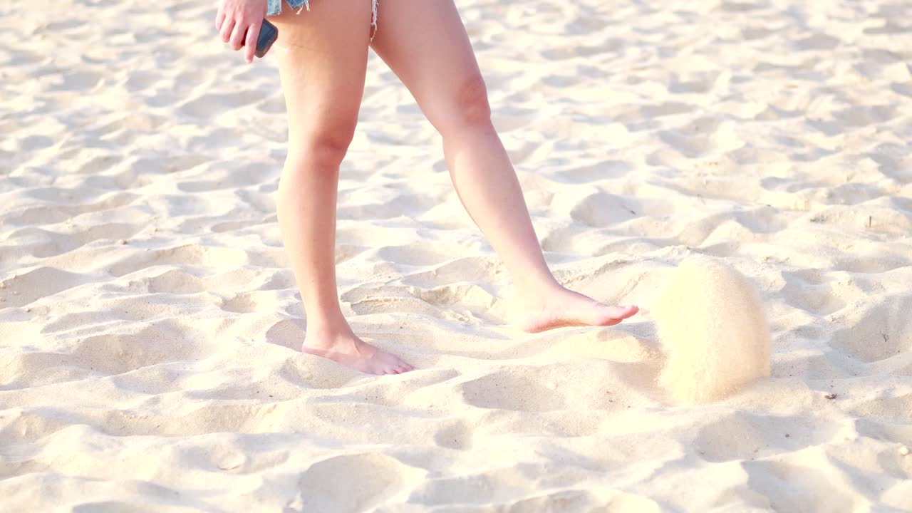Donna che calcia giocosamente la sabbia su una soleggiata spiaggia di Phuket in Thailandia.