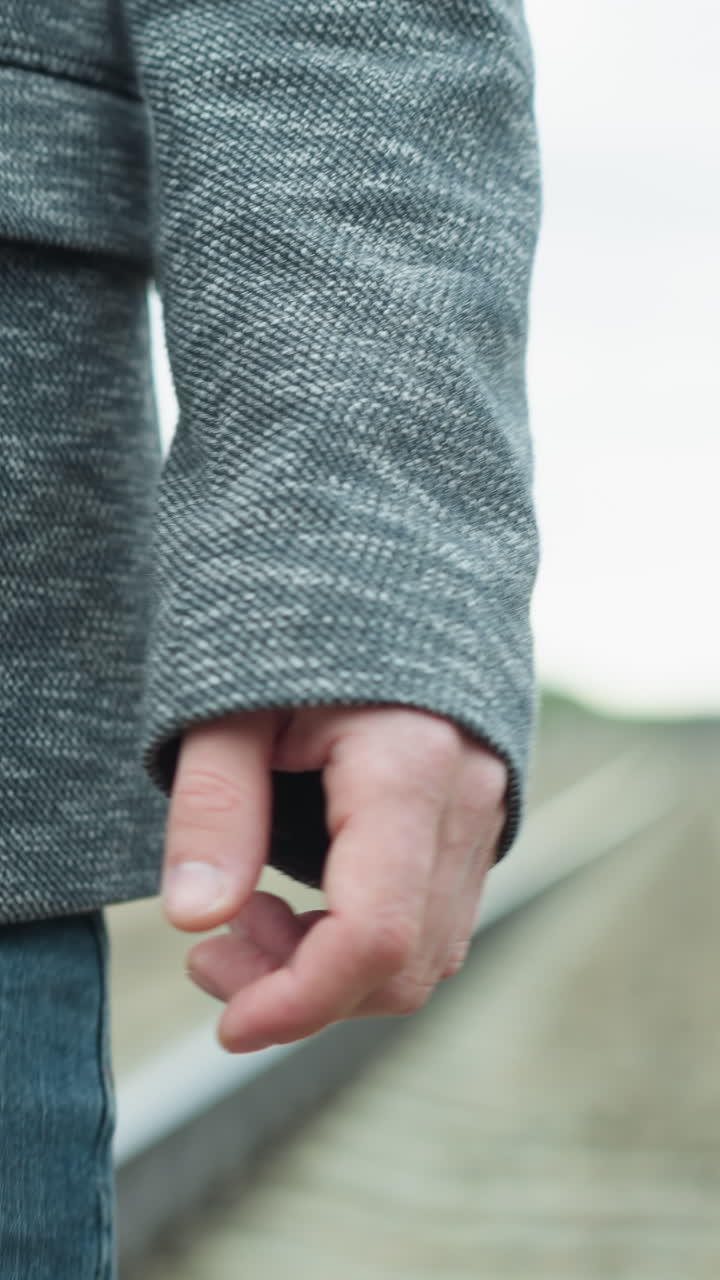 회색 슈트와 검은색 폴로 셔츠를 입은 남자가 철도 트랙을 고 주변이 흐릿한 모습으로 그의 옷에는 회색 블레이저와 파란 청바지가 포함되어 있습니다.