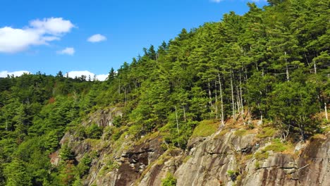 aerial footage pull back from lone climber at the top of cliff in maine revealing blue skies and clouds