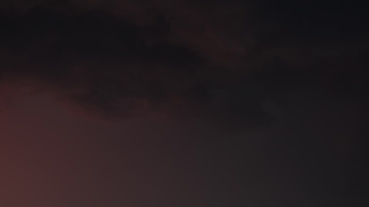 Thunderstorm clouds glow red in setting sun, stormy sky at night