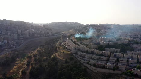 aerial view of a hilly cityscape with rising smoke and a separation wall