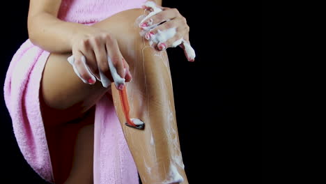 a young woman shaving her leg with a razor blade and shaving foam wearing a pink towel.