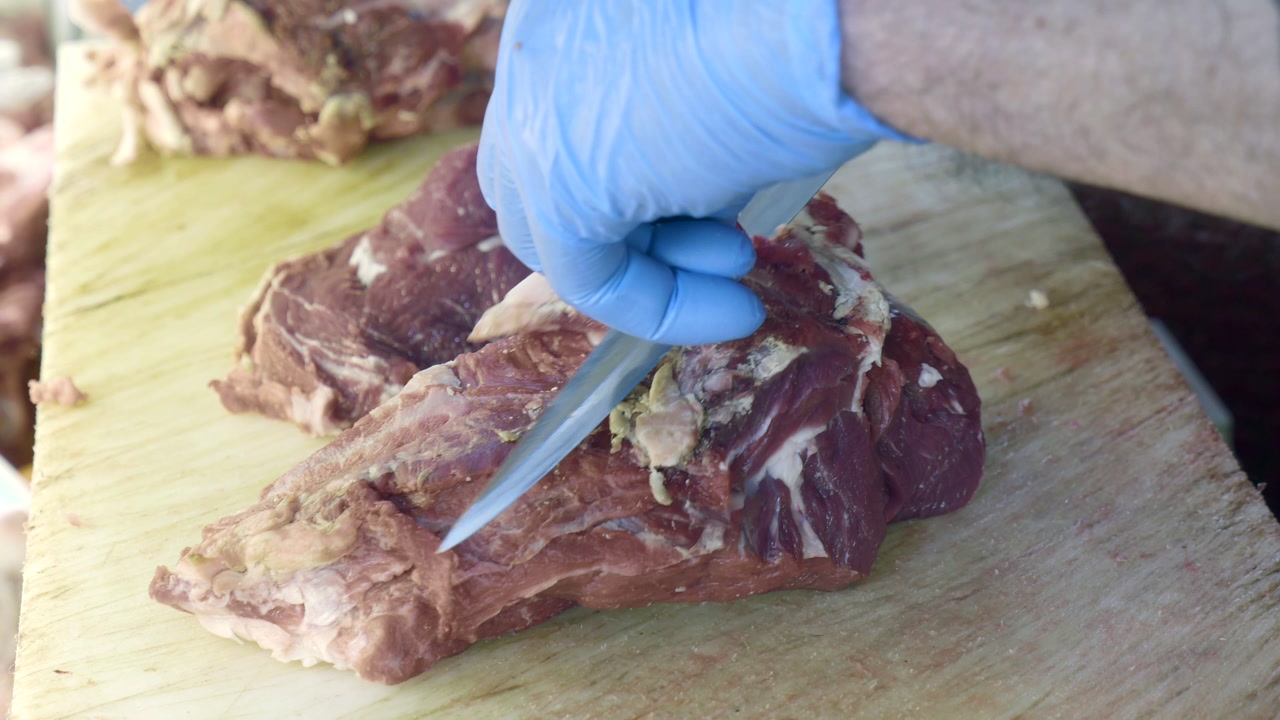 Professional Butcher Trimming Raw Meat with a Knife