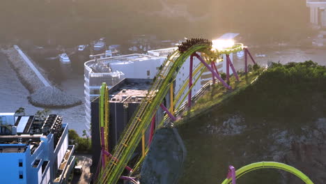 Orbiting-aerial-drone-tele-lens-shot-of-'Hair-Raiser'-rollercoaster-in-Ocean-Park,-Hong-Kong,-with-Aberdeen-typhoon-shelter-in-backdrop