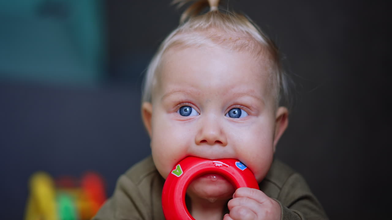 Beautiful Caucasian baby with blond hair and blond hair. Close up. Lovely infant chewing the toy for dentition.