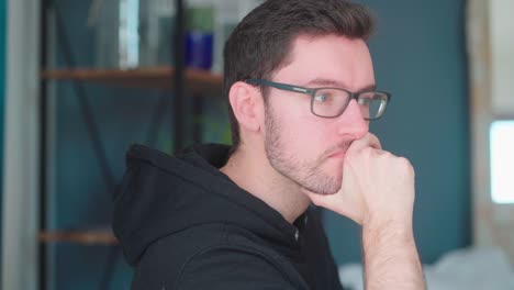 pensive young man sitting pondering in living room