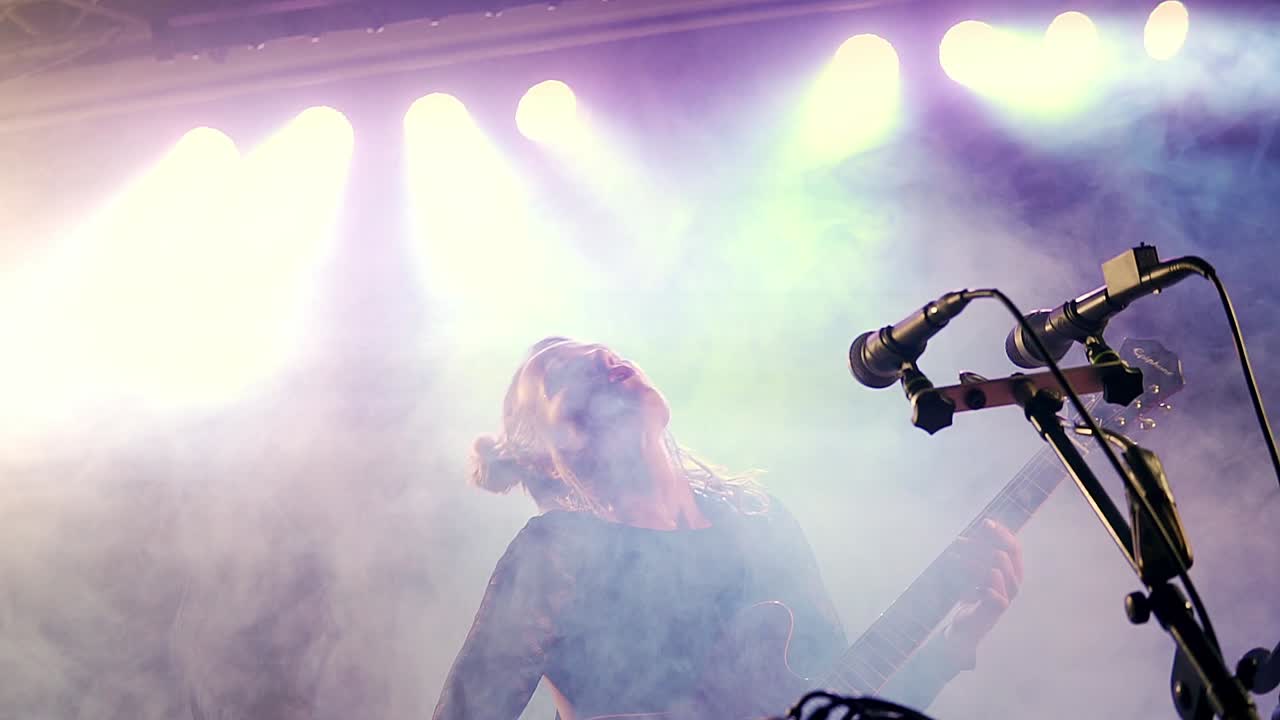 joven intérprete hermosa con una guitarra cantando en el escenario con un fondo de iluminación colorido